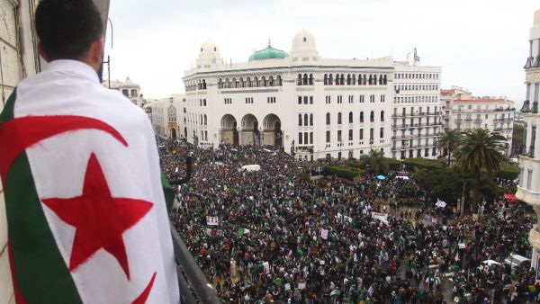 An Algerian man draped in a national flag watches as protesters gather for a demonstration against ailing President Abdelaziz Bouteflika in front of La Grande Poste. (AFP)