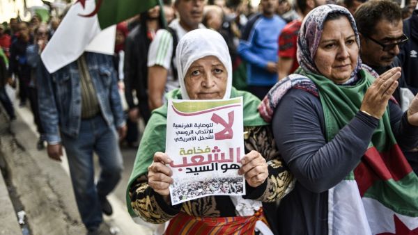 An elderly Algerian protester holds up a sign reading in Arabic "no to French guardianship, to Russian mandate, to US intervention; its excellency, the People, is master" as she marches with others draped in the national flag march during the 36th consecutive Friday anti-government demonstrations in the capital Algiers, on October 25, 2019. (RYAD KRAMDI / AFP)