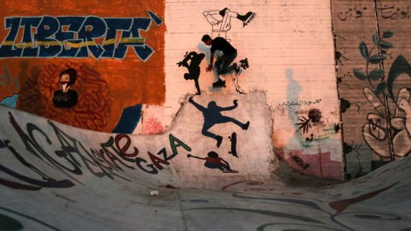 Palestinian youths play with rollerblades by walls covered with graffiti at the sea port in Gaza City on 19 June, 2018. [MAHMUD HAMS/AFP]