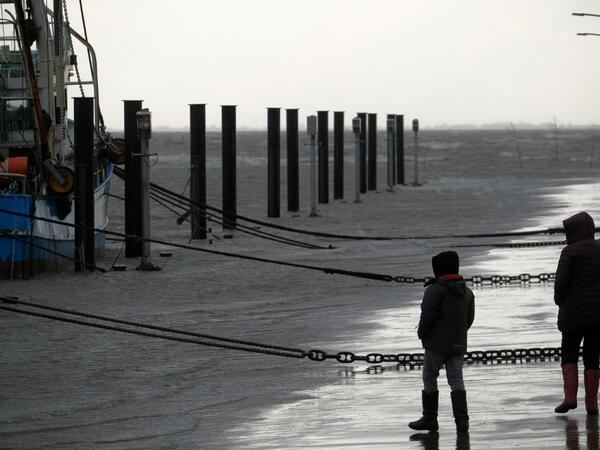 People walk near fish trawlers at the flooded harbor of Wremen, on the North Sea near Bremerhaven, northern Germany, on Febuary 11, 2020. Fierce winds and heavy rains claimed at least six lives across northern Europe on February 11, 2020, as Storm Ciara disrupted travel, grounded hundreds of flights, flooded roads and left vast areas without power. Patrik Stollarz / AFP