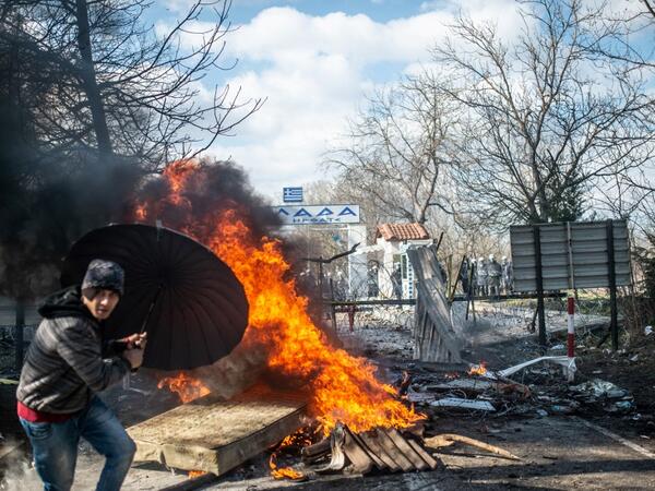 A man takes coover behind an umbrella as he throws a mattress in a fire during clashes with Greek police in the buffer zone at Turkey-Greece border, at Pazarkule, in Edirne district, on February 29, 2020. BULENT KILIC / AFP