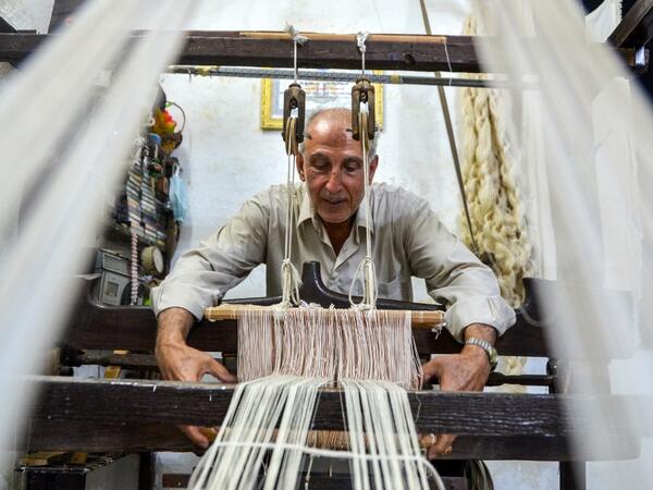 Muhammad Saud, a 65-year-old Syrian silk farmer, handweaves silk threads on a loom at his home workshop in the village of Deir Mama, in west-central Syria on June 22, 2020. MAHER AL MOUNES / AFP