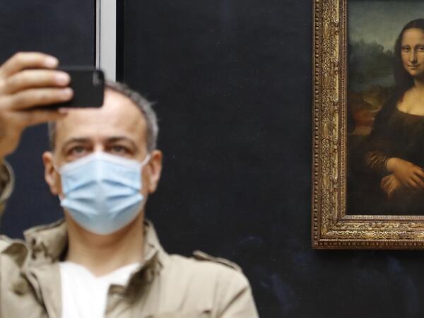 A visitor wearing a protective face mask takes a selfie in front of Leonardo da Vinci's masterpiece "Mona Lisa" also known as "La Gioconda" on the reopening day of the Louvre Museum in Paris on July 6, 2020. FRANCOIS GUILLOT / AFP