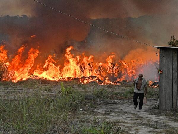 An elderly farmer who set fire to rainforest around his property walks away as the fire approaches their house in an area of Amazon rainforest, south of Novo Progresso in Para state, Brazil, on August 15, 2020. CARL DE SOUZA / AFP