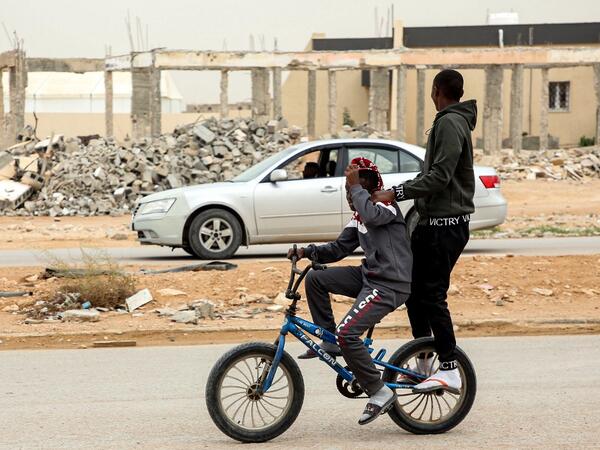 A boy rides behind another on a bicycle along a road past destroyed buildings in the city of Tawergha, some 200 kilometres (125 miles) east of Libya's capital close to the port city of Misrata, on December 12, 2020. When Libyan dictator Moamer Kadhafi was toppled, people took revenge on those they saw as his supporters -- including the entire town of Tawergha, whose 40,000 residents were forced to flee. Now, almost a decade later since militia forces rampaged through the town torching homes, destroying buil