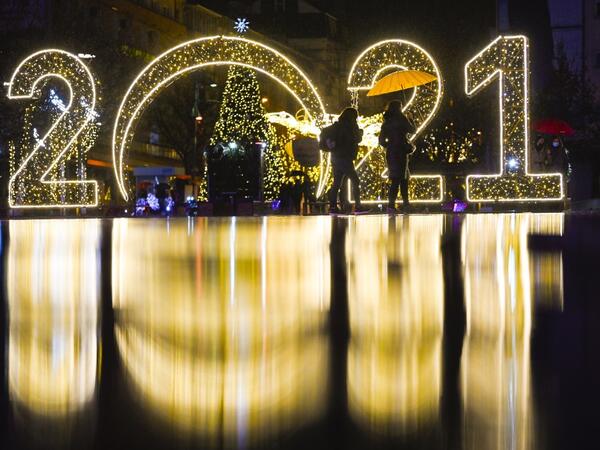 Women walk under an umbrella in front of a 2021 sign displayed in downtown Pristina on December 30, 2020, as Kosovars prepare to celebrate the New Year 2021 at their homes, amid the ongoing Covid-19 (novel coronavirus) pandemic. Armend NIMANI / AFP