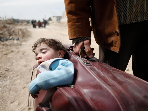 On 15 March 2018 in Beit Sawa, eastern Ghouta, a man carrying a child in a suitcase walks towards Hamourieh where an evacuation exit from eastern Ghouta has been opened.