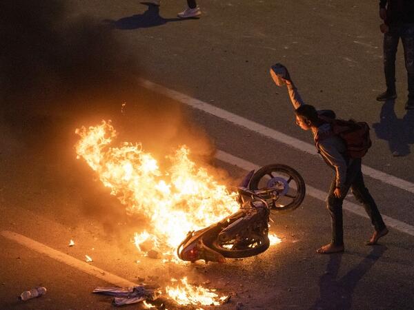 A migrant throws a rock onto a burning motorbike as they clash with Moroccan riot police in protest at being stopped from crossing the border, in the northern town of Fnideq, close to the border between Morocco and Spain's North African enclave of Ceuta on May 19, 2021. Migrants were still trying to cross from Morocco into the Spanish enclave of Ceuta on May 19, 2021, after a record 8,000 people poured over the border this week, escalating tensions between Rabat and Madrid. 