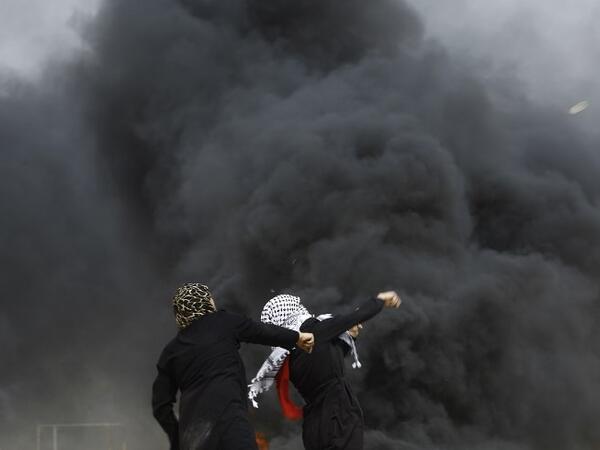 Palestinian women attend throw stones past smoke plume rusing from burning tires during clashes with Israeli forces across the border, following a demonstration calling for the right to return -- meaning Palestinian refugees being allowed to go back to the land they fled or were expelled from during the 1948 war surrounding Israel's creation -- near the border with Israel, east of Gaza City, in the southern Gaza Strip, on Apr. 20, 2018. 
(MOHAMMED ABED / AFP)