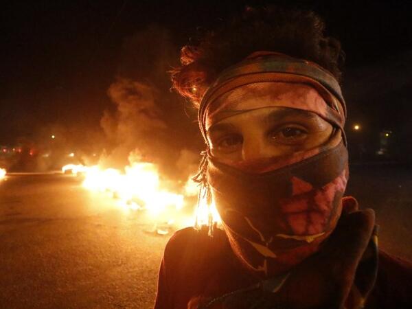 A masked demonstrator participates in an ongoing protest against unemployment and high cost of living as others burn tyres in the southern Iraqi city of Basra during the night of July 12, 2018. (AFP/Haidar Mohammad Ali)
