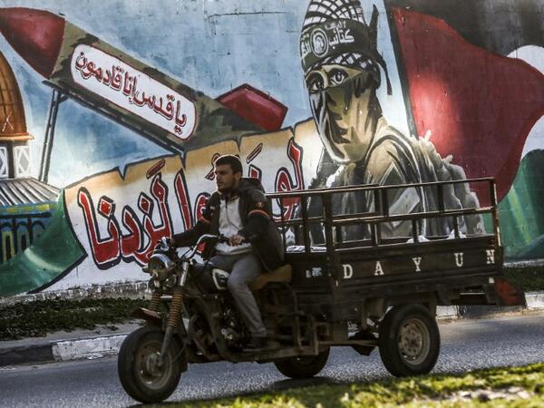 A Palestinian drives a motorcycle cart past a mural depicting a masked fighter of the Qassam Brigades, the armed wing of the Hamas movement, next to a missile with a caption reading in Arabic "Oh Jerusalem, we are coming" and the Dome of the Rock, in a street in Rafah in the southern Gaza Strip 
SAID KHATIB / AFP