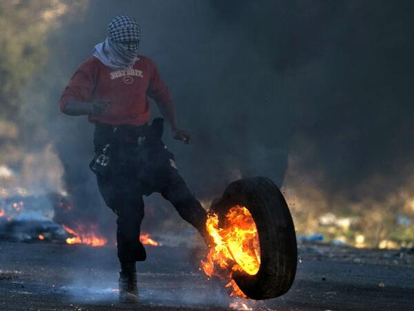 A Palestinian protestor kicks a burning tire towards Israeli security forces during clashes in the West Bank city of Nablus, following a demonstration against US President Donald Trump's decision to recognize Jerusalem as the capital of Israel on Dec. 9, 2017. 
(JAAFAR ASHTIYEH / AFP)