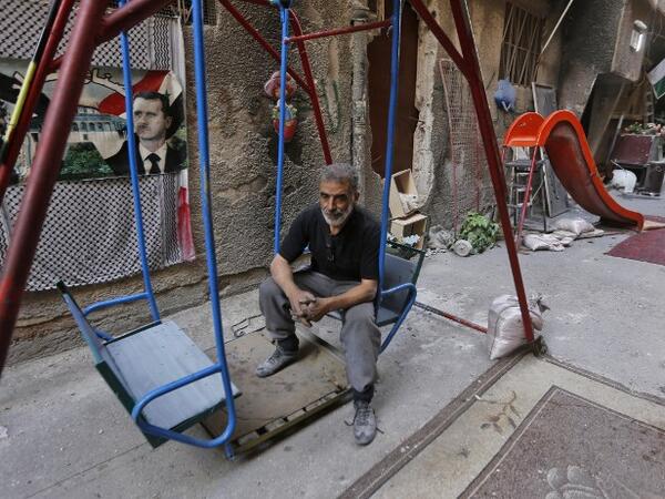 A man sits on a swing next to images of the late Palestinian leader Yasser Arafat and the Syrian President Bashar al-Assad in Yarmuk camp southern Damascus on November 1, 2018. 
LOUAI BESHARA / AFP