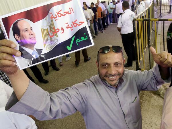 An Egyptian man, living in Kuwait, gives the thumbs up as he waves a placard bearing the portrait of President Abdel Fattah al-Sisi before casting his vote in a referendum on constitutional amendments, at the Egyptian embassy in Kuwait City on April 19, 2019. AFP
