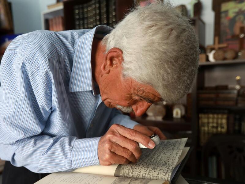 George Zaarour, a specialist in the Aramaic language, uses a magnifying glass to decipher Aramaic script in the Syrian mountain village of Maalula, in the Damascus region on May 13, 2019. LOUAI BESHARA / AFP