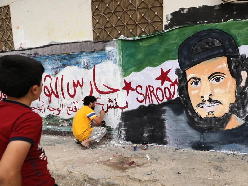 A child watches as a local artist works on a mural painting showing the late Syrian rebel fighter Abdel-Basset al-Sarout in the town of Binnish in the jihadist-held northern Idlib province on June 8, 2019. OMAR HAJ KADOUR / AFP