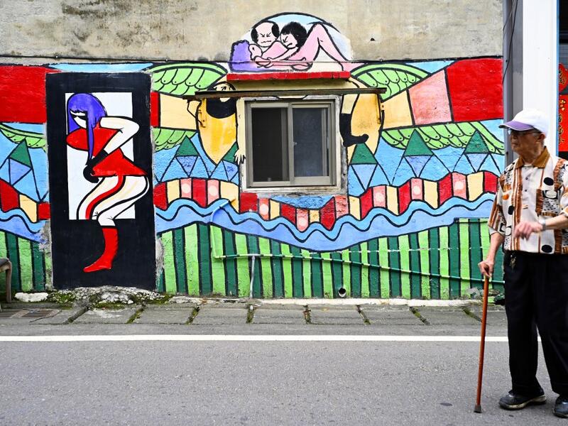 This picture taken on March 30, 2019 shows a local resident walking past a wall painted by Hakka graffiti artist Wu Tsun-hsien in the Taiwanese village of Ruan Chiao. Nestled in the mist-covered foothills of Taiwan's central mountain range, Ruan Chiao village is virtually devoid of young people, but artist Wu Tsun-hsien is coaxing the Instagram generation back by transforming local homes into a canvas of colour. Sam YEH / AFP