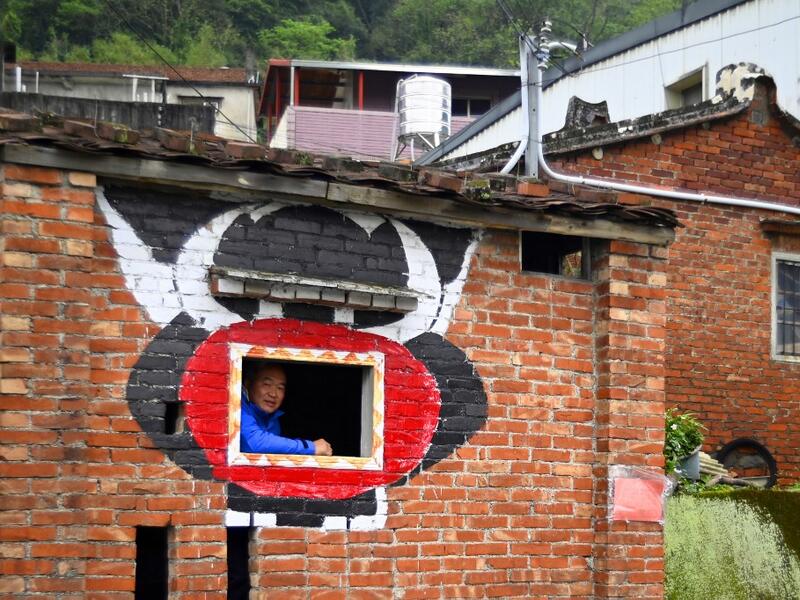 This picture taken on March 30, 2019 shows Hakka graffiti painter Wu Tsun-hsien posing for a photo in a empty old house near his home in the Taiwanese village of Ruan Chiao. Nestled in the mist-covered foothills of Taiwan's central mountain range, Ruan Chiao village is virtually devoid of young people, but artist Wu Tsun-hsien is coaxing the Instagram generation back by transforming local homes into a canvas of colour. Sam YEH / AFP