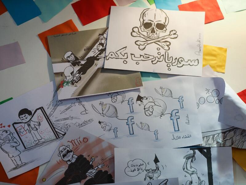 This picture shows illustrations by Syrian Cartoonist Amani al-Ali at her home studio in the city of Idlib in the eponymous northwestern province, including a drawing of a skull and crossbones with a caption below reading in Arabic "Syria welcomes you", and another of a woman being pulled from four sides by different men.  Omar HAJ KADOUR / AFP
