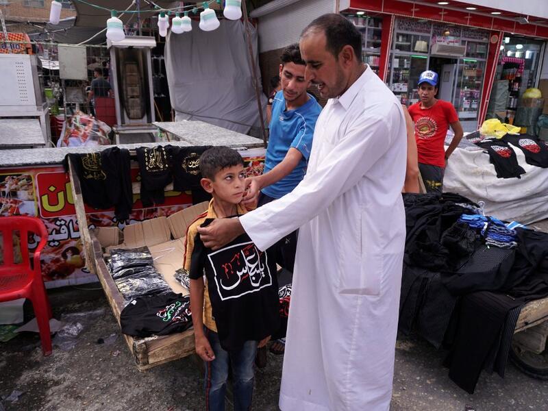 A man tries on a black t-shirt on the chest of a child, emblazoned with the Shiite Muslim slogan "O Abbas", as a sign of mourning referring to the Muslim Imam Abbas ibn Ali, grandson of the prophet Mohamed, amidst preparations ahead of the Shiite Muslim religious mourning period of Ashura, in the central Iraqi holy shrine city of Najaf on August 31, 2019.  Haidar HAMDANI / AFP