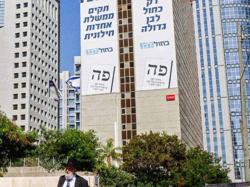 An Ultra-Orthodox Jewish man walks along a street in the Israeli coastal city of Tel Aviv on September 12, 2019, as electoral billboards are seen in the background off the facade of a building showing the faces of (L to R) Yair Lapid and retired general Benny Gantz, two of the leaders of the "Blue and White" (Kahol Lavan) electoral alliance vying for seats in the upcoming September 17 vote. Gil COHEN-MAGEN / AFP