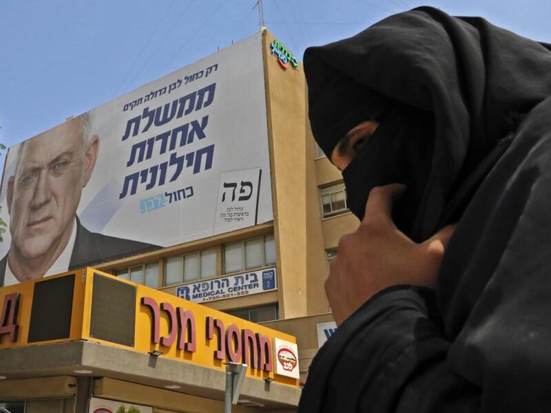 A Bedouin woman walks below an electoral banner for the Blue and White (Kahol Lavan) electoral alliance bearing the portrait of retired general Benny Gantz with a caption in Hebrew reading "only with the Blue and White we will create a united secular government" in the southern Israeli city of Beersheva on September 15, 2019. HAZEM BADER / AFP