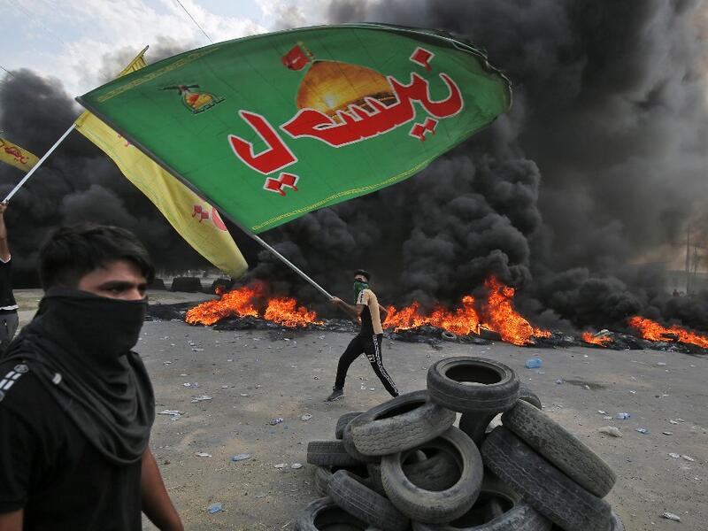 An Iraqi protester waves an Iraqi Hezbollah flag during a demonstration against state corruption, failing public services and unemployment in the Baladiyat district of the capital Baghdad on October 2, 2019. Iraq's president and the United Nations urged security forces to show restraint after two protesters were killed in clashes with police that other top officials blamed on "infiltrators." AHMAD AL-RUBAYE / AFP