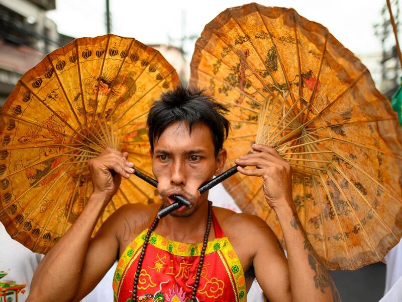 A devotee of a Chinese shrine with two umbrellas pierced through his cheeks takes part in a procession during the annual Vegetarian Festival in Phuket on October 5, 2019. Mladen ANTONOV / AFP