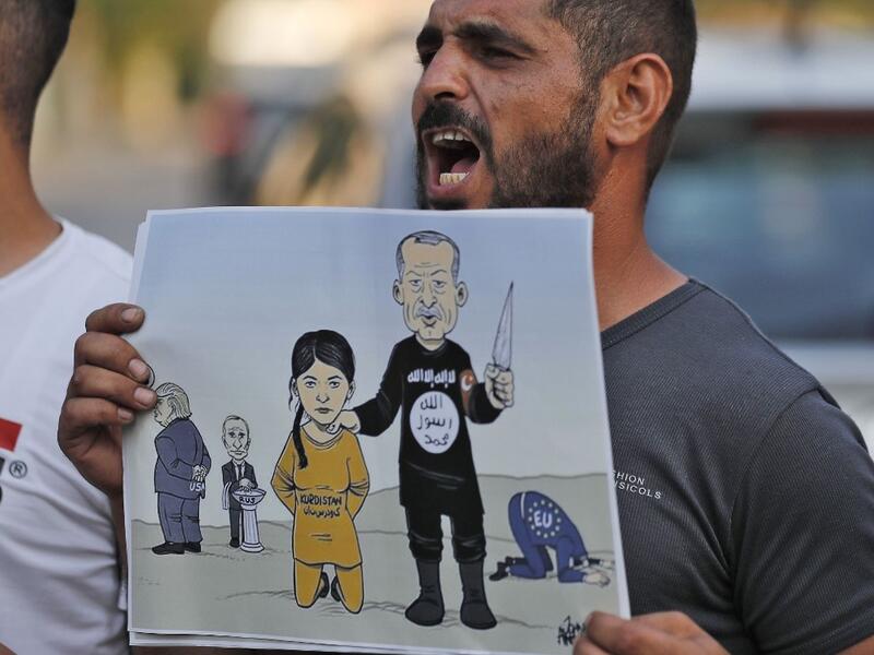 A man shouts slogans while holding up a sign showing a cartoon depicting current Turkish President Recep Tayyip Erdogan dressed in an Islamic State (IS) group uniform showing the group's logo and holding up a knife next to a woman dressed in an orange jumpsuit reading "Kurdistan"  (AFP)