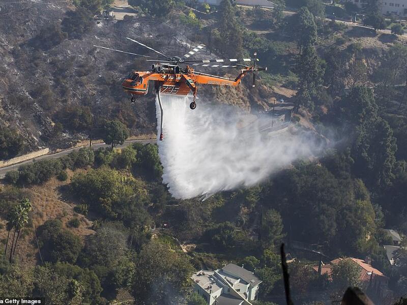 A helicopter drops water on houses on fire in Brentwood on Monday as fires continue to ravage California. (AFP)