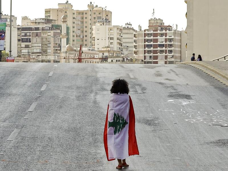 A Lebanese woman protester walks draped in a national flag along the Fuad Chehab avenue, near the Martyrs' Square, in the centre of the capital Beirut on October 29, 2019. (AFP/ File Photo) A Lebanese woman protester walks draped in a national flag along the Fuad Chehab avenue, near the Martyrs' Square, in the centre of the capital Beirut on October 29, 2019. (AFP/ File Photo)