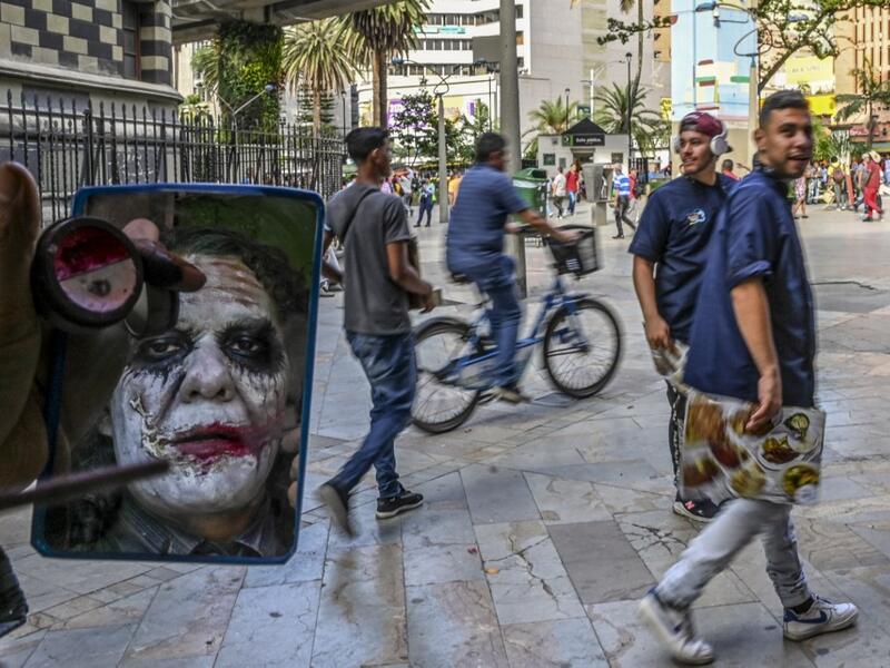 Venezuelan migrant Johnny Tales, who makes a living imitating the comicbook and film character "The Joker", applies make up as he prepares to perform in downtown Medellin, on October 28, 2019. JOAQUIN SARMIENTO / AFP