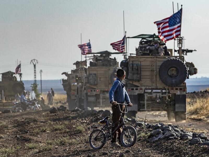 A Syrian boy on his bicycle looks at a convoy of US armoured vehicles patrolling fields near the northeastern town of Qahtaniyah at the border with Turkey, on October 31, 2019. US forces accompanied by Kurdish fighters of the Syrian Democratic Forces (SDF) patrolled part of Syria's border with Turkey, in the first such move since Washington withdrew troops from the area earlier this month, an AFP correspondent reported. Delil SOULEIMAN / AFP