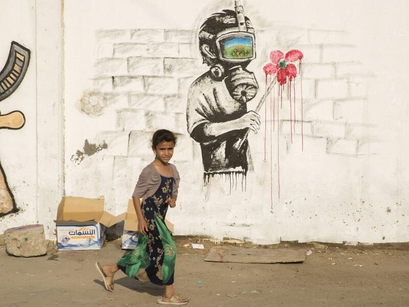 An Iraqi girl walks past a mural during ongoing anti-government demonstrations in the southern city of Basra on October 31, 2019. Iraqi security forces are using skull-piercing tear gas canisters against protesters, killing at least five in an "unprecedented" use of the weapon, Amnesty International said. Anti-government demonstrations have rocked the Iraqi capital and its south this month, leaving more than 250 people dead so far -- around half of them in the capital.   Hussein FALEH / AFP