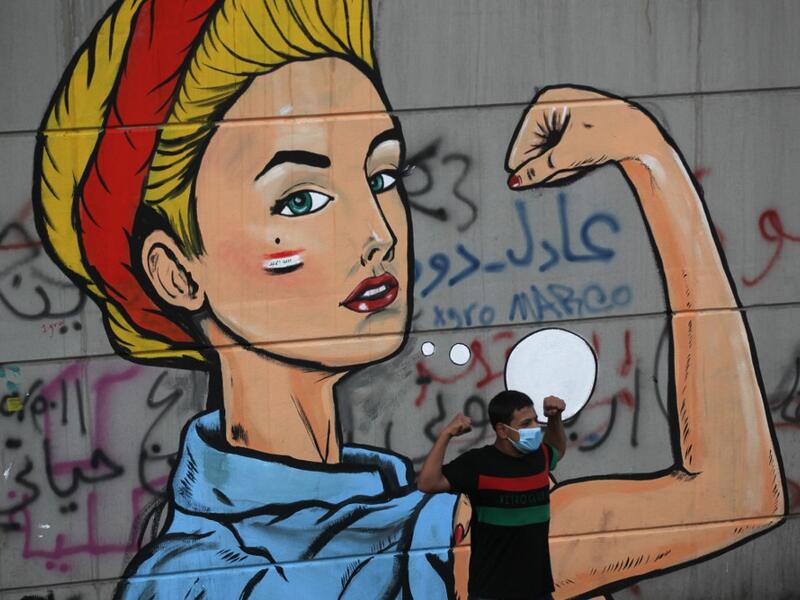 An Iraqi protester poses in front of a mural at Baghdad's Tahrir square during ongoing anti-government demonstrations on November 2, 2019. Iraqi security forces clashed with anti-government protesters in the early hours of Saturday near the capital's Tahrir Square, leaving one demonstrator dead and dozens more wounded, medical sources said. AHMAD AL-RUBAYE / AFP