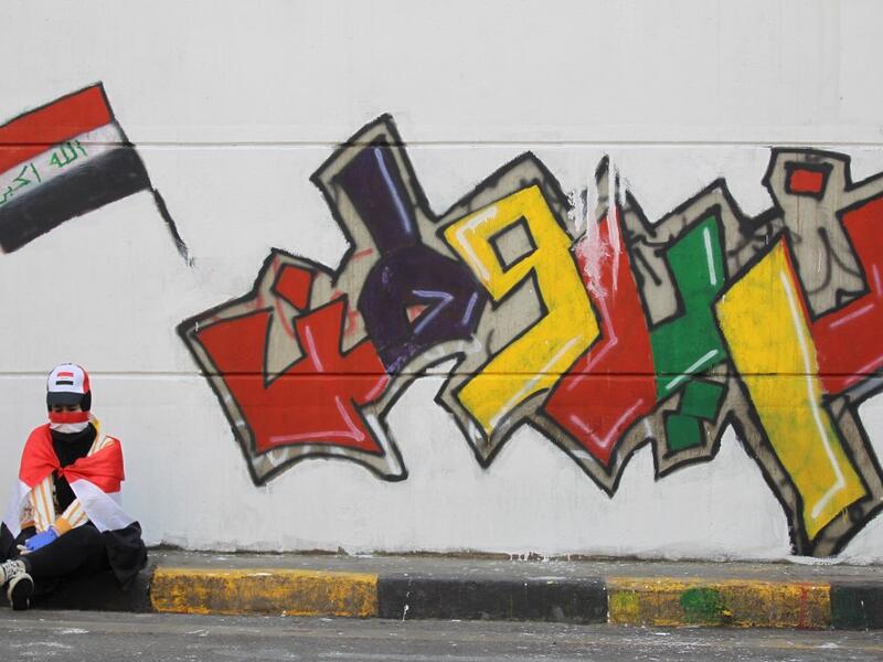 An Iraqi demonstrator clad with the national flag rests in front of a mural which reads "we want a homeland", amid ongoing anti-government protests in the capital Baghdad on November 3, 2019. Protesters in Iraq's capital and the country's south shut down streets and government offices in a new wave of civil disobedience, escalating their month-long movement demanding wholesale change of the political system. AHMAD AL-RUBAYE / AFP
