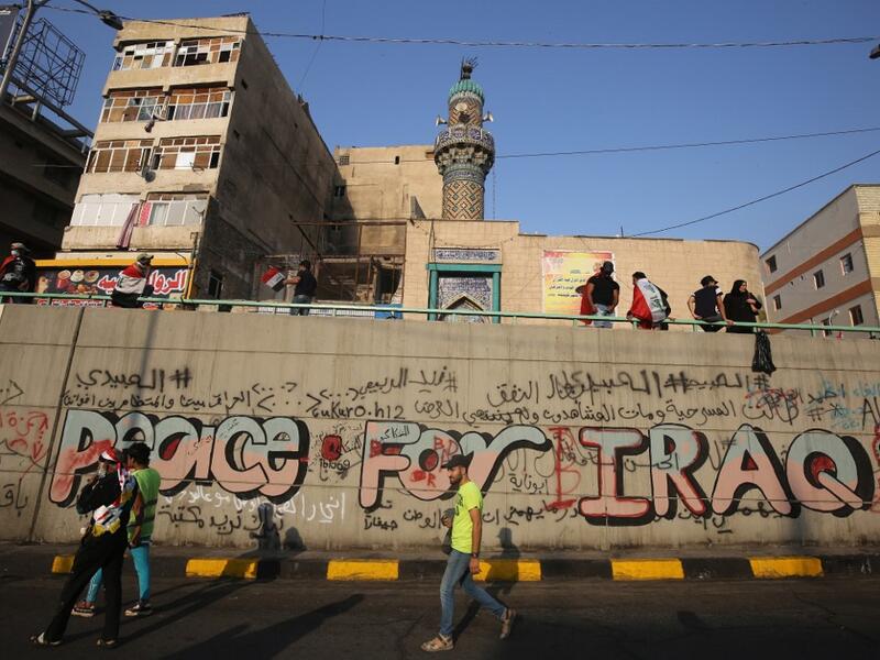 Iraqi demonstrators walk by a graffiti-filled wall in Tahrir square in the capital Baghdad on November 3, 2019, amid ongoing anti-government protests. Protesters in Iraq's capital and the country's south shut down streets and government offices in a new wave of civil disobedience, escalating their month-long movement demanding wholesale change of the political system. AHMAD AL-RUBAYE / AFP