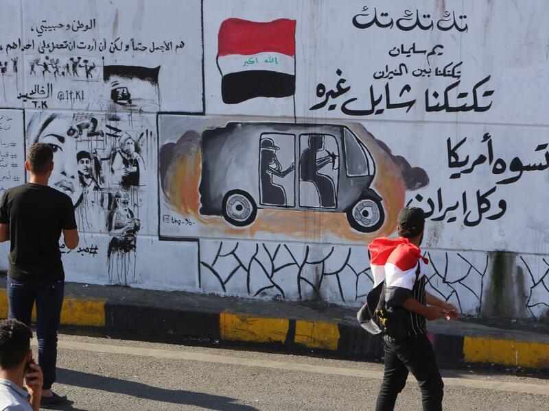 Iraqis walk past graffiti hailing Iraq's tuk-tuk drivers who have been helping protesters in Baghdad's Tahrir square, as the Iraqi capital braces for another day of protests on November 6, 2019. Arabic slogans on the wall read: "Our Tuk-tuk drivers are in the fire, they help others.. they are better than America and Iran together." The drivers of the motorised rickshaws, typically seen in poorer parts of the capital, have become the unofficial heros of the protest movement. SABAH ARAR / AFP
