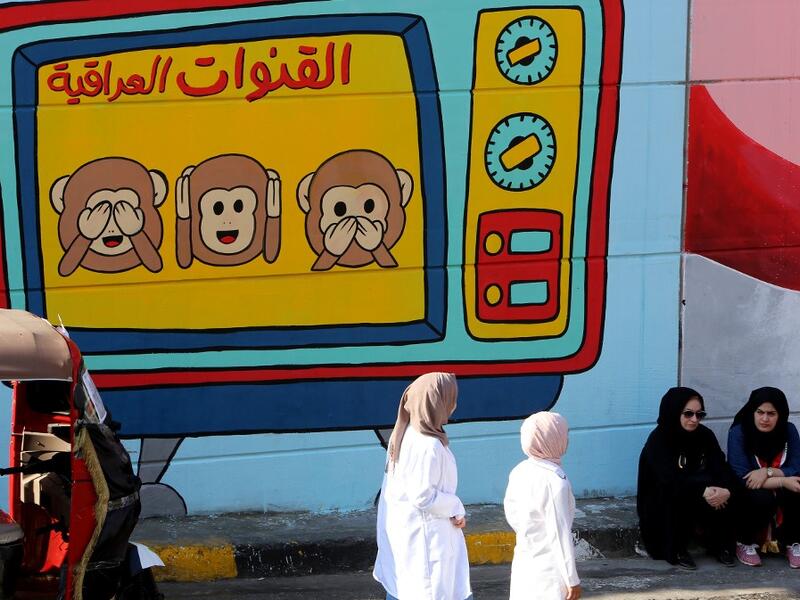 Iraqi women are pictured in front of a colourful mural in Baghdad on November 6, 2019 representing Iraqi TV channels, "that do not want to see, hear or speak about" the anti-government protests that have engulfed Iraq since early October. A mounting death toll in Baghdad and across southern Iraq coupled with renewed internet restrictions sparked fears that anti-government protests would once again trigger chaos. SABAH ARAR / AFP
