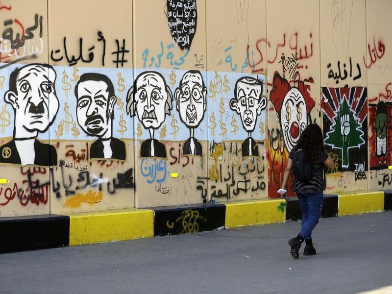 A woman walks past graffitis sprayed on a wall in Lebanon's capital Beirut on November 6, 2019. Since October 17, the chanting of tens of thousands of Lebanese denouncing the political elite have shaken the normally staid district around two Beirut squares, Martyrs' and Riad Al Solh. JOSEPH EID / AFP