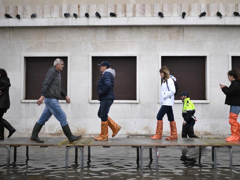 People walk on a footbridge across a flooded street after an exceptional overnight "Alta Acqua" high tide water level, on November 13, 2019 in Venice. Venice was hit by the highest tide in more than 50 years late November 12, with tourists wading through flooded streets to seek shelter as a fierce wind whipped up waves in St. Mark's Square. Marco Bertorello / AFP
