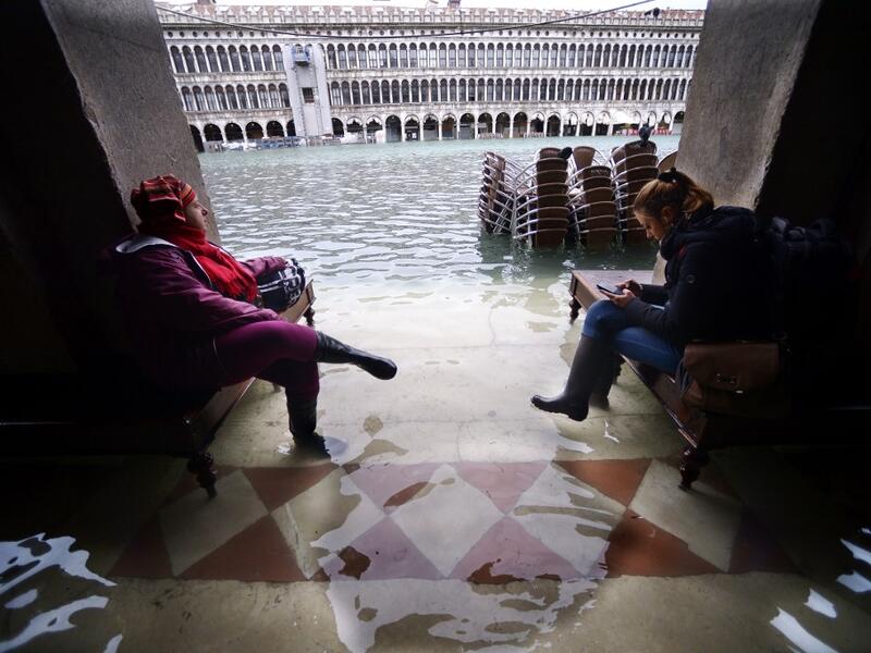 People sit on benches in a flooded arcade by St. Mark's Square on November 15, 2019 in Venice, two days after the city suffered its highest tide in 50 years. Flood-hit Venice was bracing for another exceptional high tide on November 15, as Italy declared a state of emergency for the UNESCO city where perilous deluges have caused millions of euros worth of damage. Filippo MONTEFORTE / AFP
