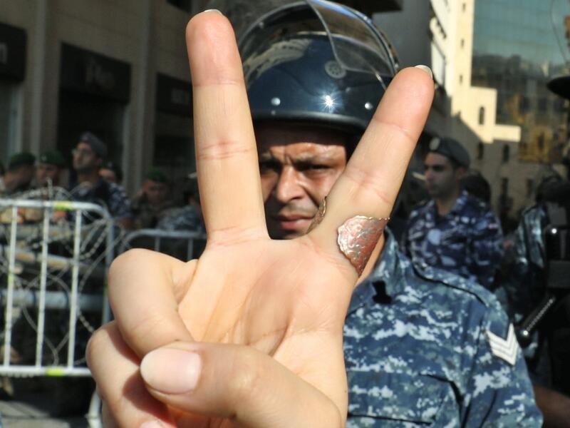 A Lebanese protester flashes the victory gesture while standing before a riot policeman at a security barrier across a road leading to the parliament headquarters during a demonstration in the capital Beirut's downtown district on November 19, 2019. An unprecedented protest movement against the ruling elite entered its second month with the country in the grip of political and economic turmoil. The leaderless pan-sectarian movement has swept the Mediterranean country since October 17, prompting the resignation of Prime Minister Saad Hariri's government. ANWAR AMRO / AFP A Lebanese protester flashes the victory gesture while standing before a riot policeman at a security barrier across a road leading to the parliament headquarters during a demonstration in the capital Beirut's downtown district on November 19, 2019. An unprecedented protest movement against the ruling elite entered its second month with the country in the grip of political and economic turmoil. The leaderless pan-sectarian movement has swept the Mediterranean country since October 17, prompting the resignat