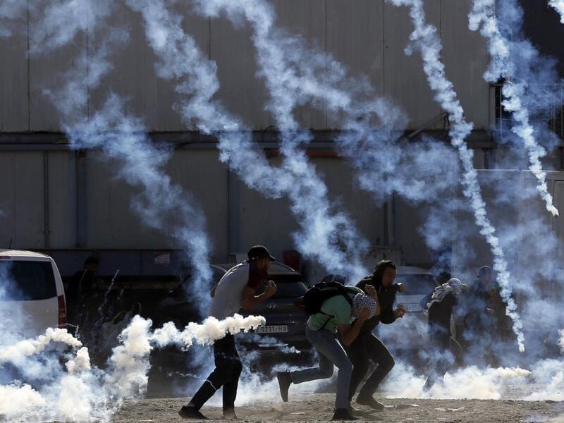 Palestinian youths run from tear gas smoke fired by Israeli security forces on November 26, 2019 during clashes in the West Bank city of Ramallah as Palestinians stage a "day of rage" against a recent US decision to no longer consider settlements in the West Bank illegal. A Palestinian convicted over the killing of three Israelis died of cancer in custody today, officials said. The death, which sparked Palestinian accusations of neglect, comes amid heightened tension with protests already scheduled in multi
