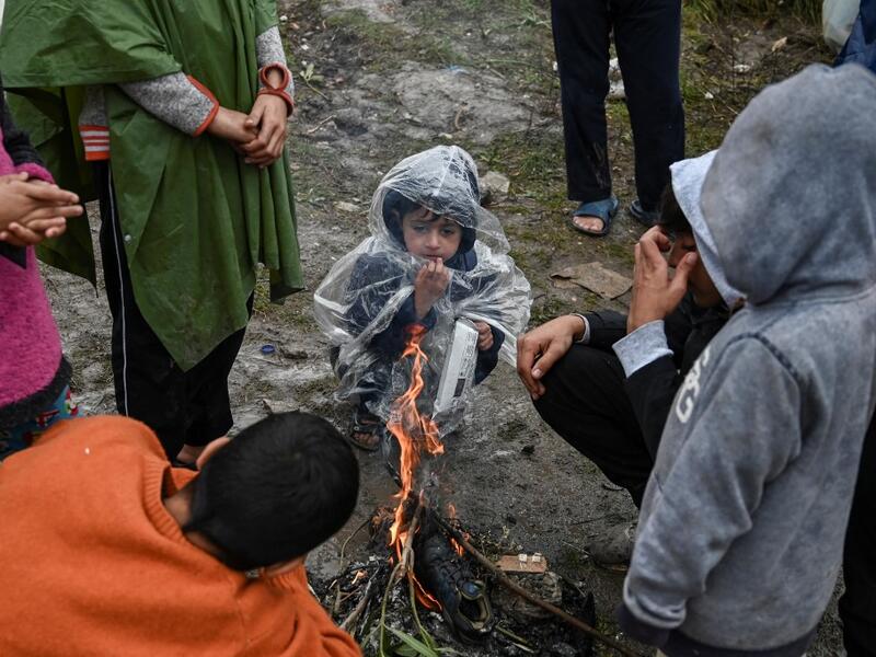 Children warm themselves around a camp fire under the rain in the refugee camp of Moria, on the island of Lesbos on November 26, 2019. Conditions remain difficult in the overcrowded Moria camp in Greece with winter fast approaching. The government announced on November 20it will shut down the three largest of its overcrowded migrant camps on islands facing Turkey, and replace them with new closed facilities with much larger capacity. ARIS MESSINIS / AFP