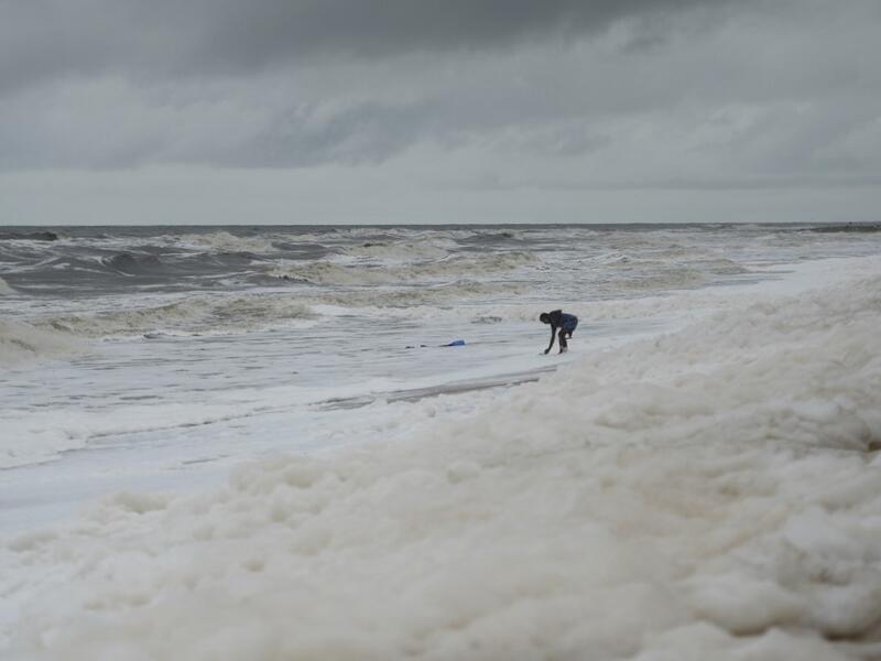 A man stands over foamy discharge, caused by pollutants, as it mixes with the surf at Marina beach in Chennai on December 1, 2019. Arun SANKAR / AFP