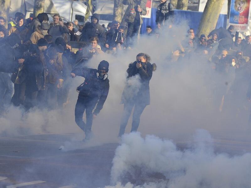 A man throws a tear canister back as people stand amid tear gas smoke during a demonstration against the pension overhauls, in Bordeaux, on December 5, 2019, as part of a national general strike. NICOLAS TUCAT / AFP