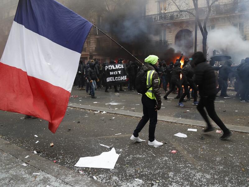 A man holding a French flag and a yellow vest walks in tear gas as protestors gesture in the background during a demonstration against the pension overhauls, in Paris, on December 5, 2019 as part of a nationwide strike. Zakaria ABDELKAFI / AFP