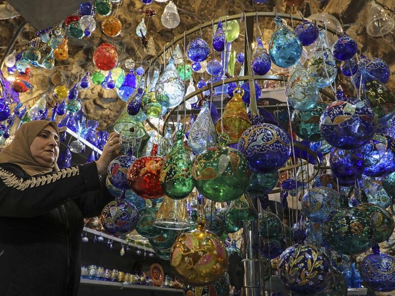 A Palestinian woman hangs glass Christmas ornaments on a display stand at a workshop in the southern West Bank city of Hebron, on December 15, 2019. HAZEM BADER / AFP