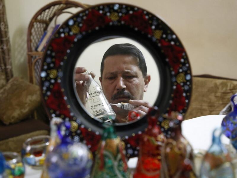 A Palestinian craftsman is reflected in a mirror as he decorates glass Christmas ornaments at a workshop in the southern West Bank city of Hebron, on December 15, 2019. HAZEM BADER / AFP